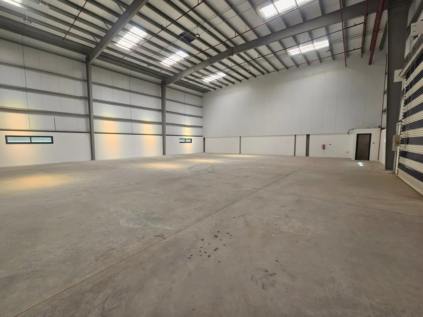 A large, empty warehouse with a concrete floor, white walls, and a high, metal ceiling.
