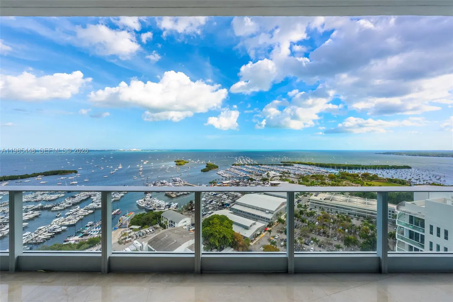 Balcony view of a marina filled with boats, a blue ocean, and a partly cloudy sky.