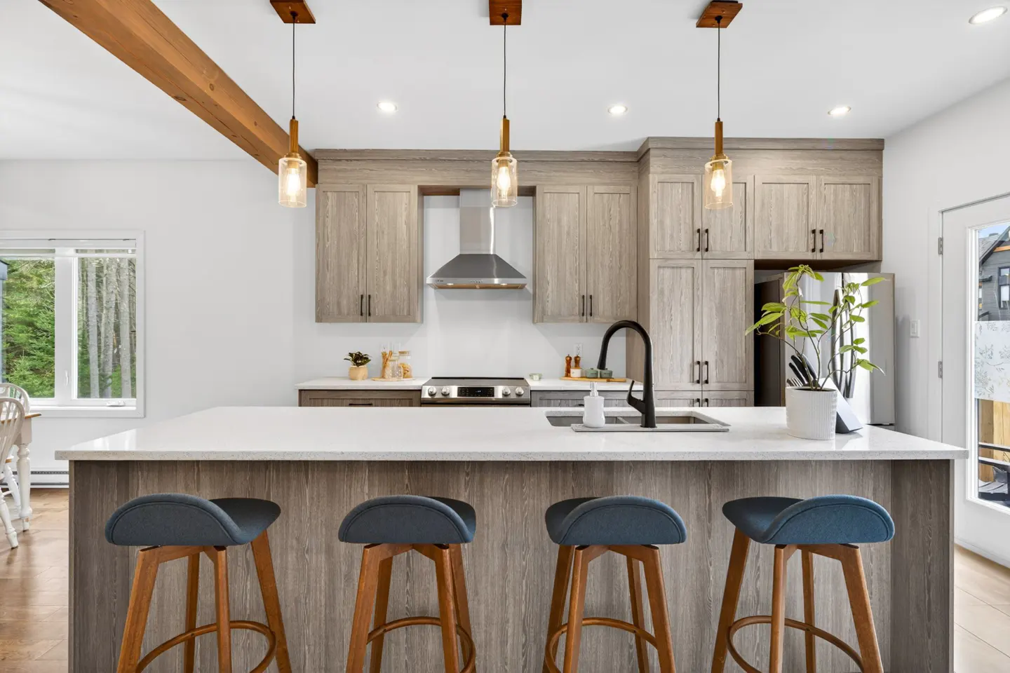 A bright kitchen with wood cabinets, a white countertop island with four blue stools, and three pendant lights.