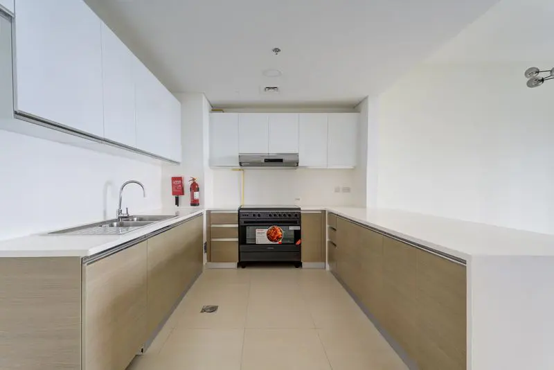 A bright, modern kitchen with white cabinets, light wood lower cabinets, and a black oven. A red fire extinguisher is mounted on the wall.