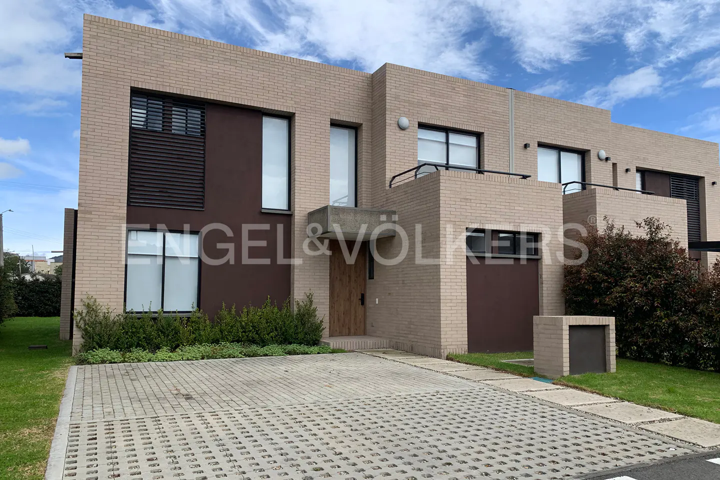 Exterior view of a modern, multi-story townhouse with a brick facade and a patterned driveway.