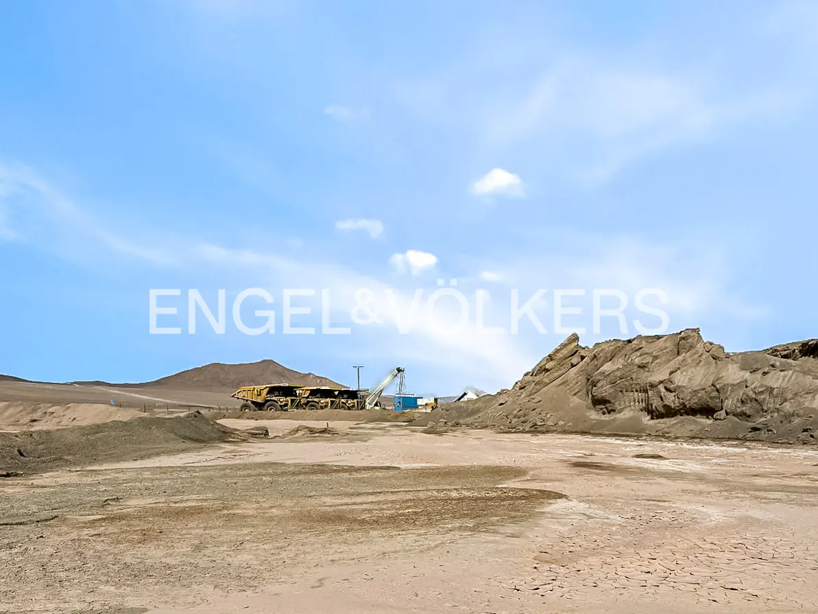 Desert landscape with mining equipment under a blue sky. A large yellow truck and a crane are visible in the distance.