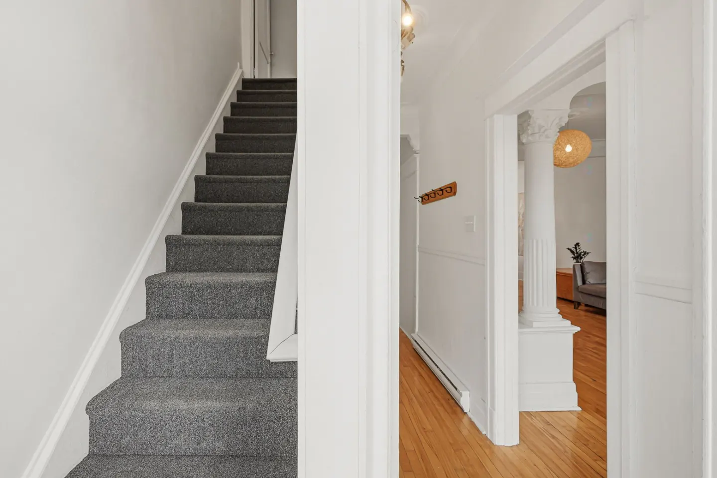 Interior view of a home featuring a gray carpeted staircase and a hallway with hardwood floors and white walls.