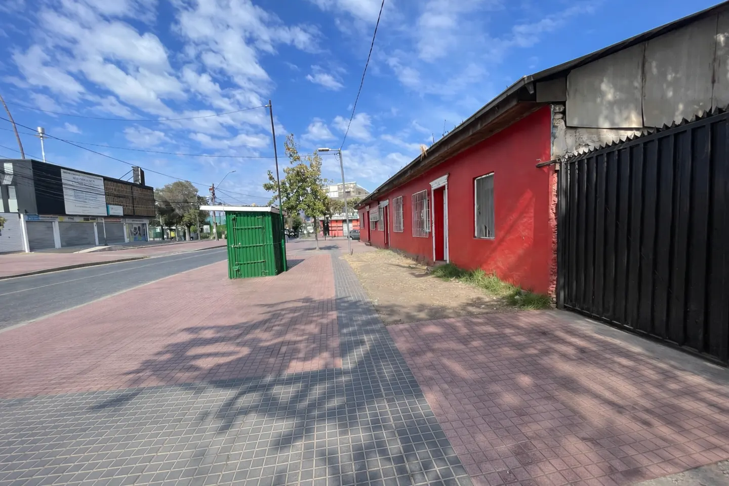 A red, one-story building with white-framed windows and doors sits behind a black metal fence on a sunny street.