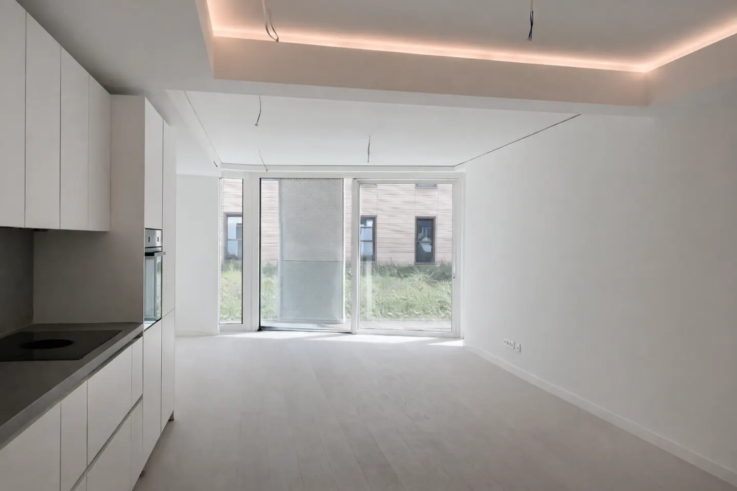 Bright, modern apartment interior with white cabinets, grey countertops, and sliding glass doors to a grassy yard.