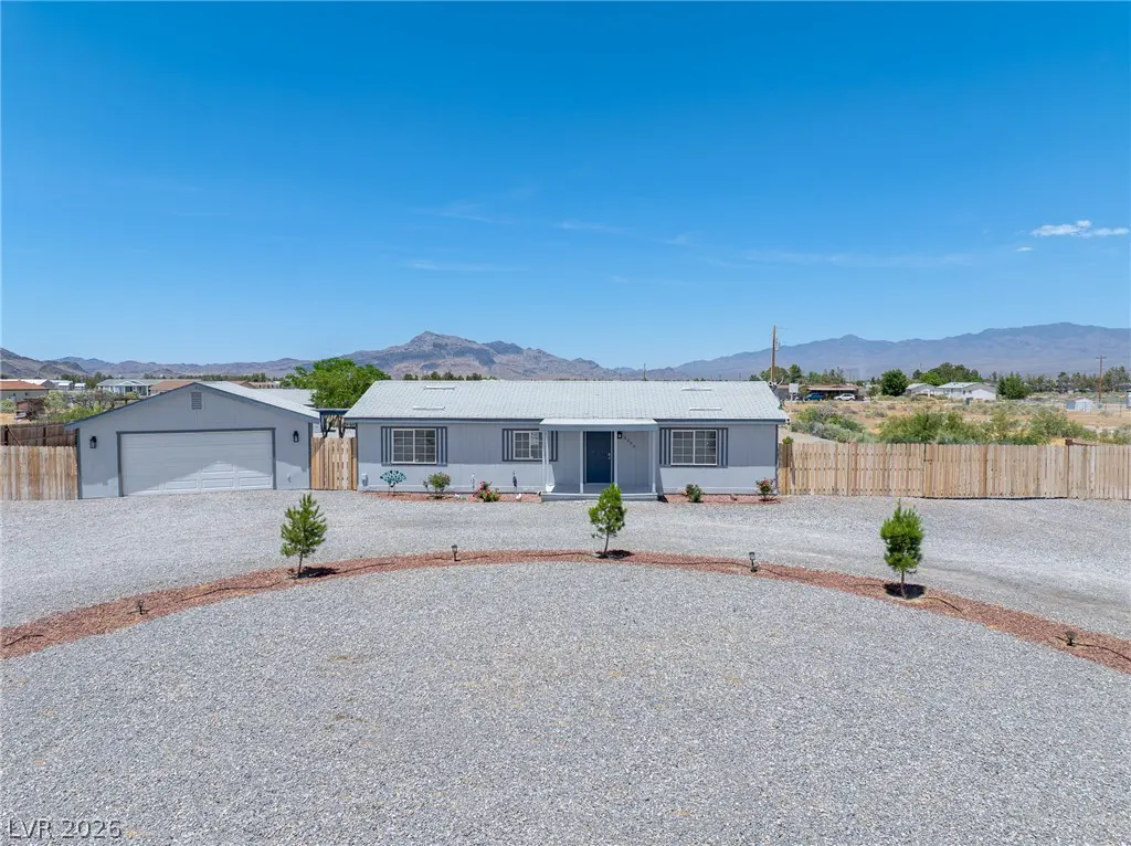 Single-story gray house with a detached garage, gravel driveway, and wooden fence against a desert mountain backdrop.