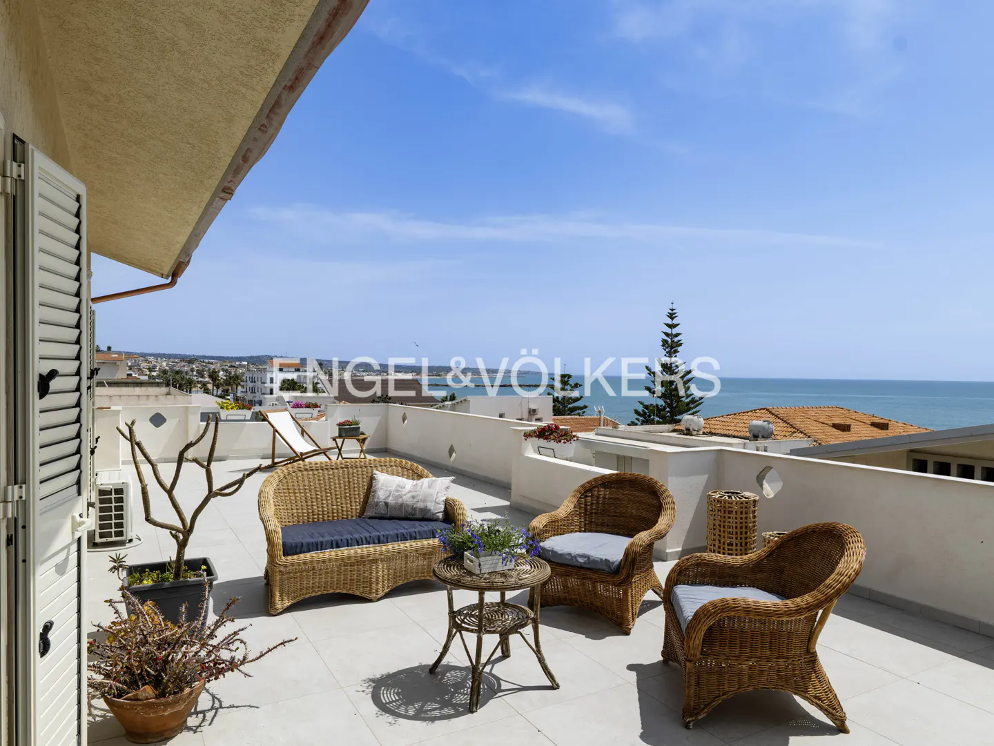 Rooftop patio with wicker furniture, blue cushions, and ocean view. Engel & Völkers logo visible.