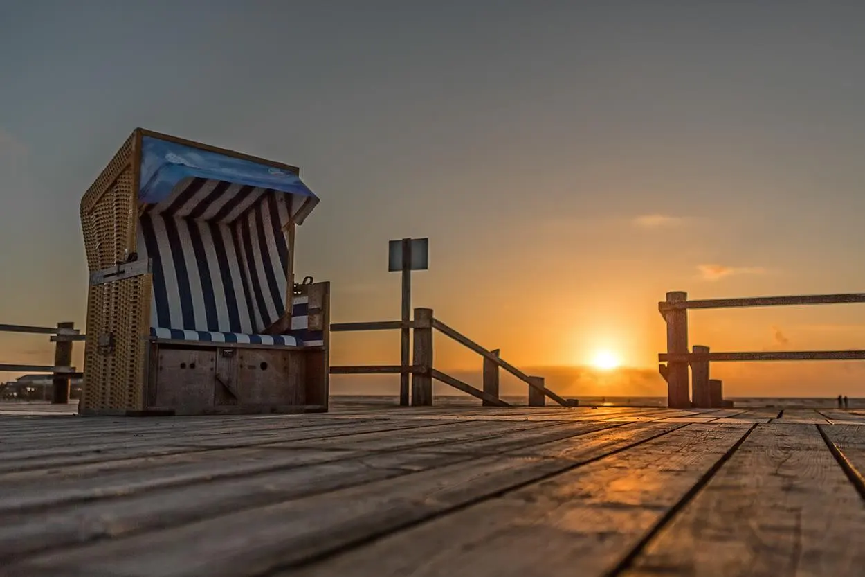 Wicker beach chair with blue and white stripes on a wooden boardwalk at sunset.