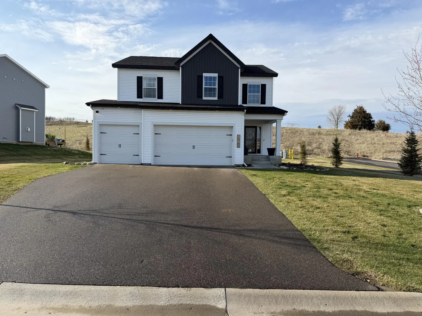 Two-story house with white siding, black trim, and a two-car garage. A black asphalt driveway leads to the house.