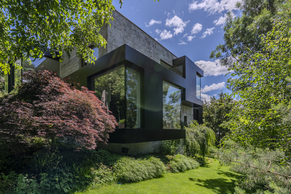 Modern home with concrete and black metal exterior, large windows, and lush garden with a red Japanese maple tree.