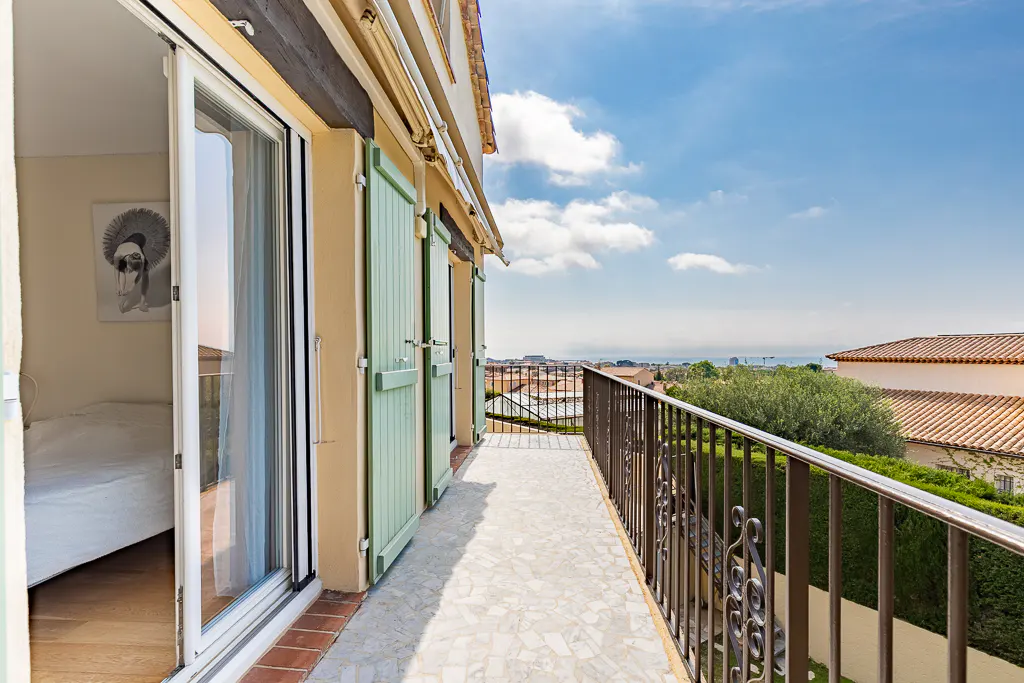 Balcony view with sliding glass doors, light green shutters, and a wrought iron railing overlooking a cityscape and blue sky.