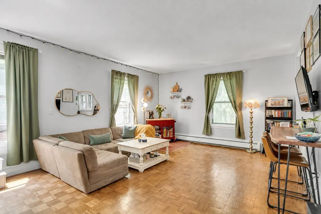 Living room with parquet floors, a beige sectional sofa, white coffee table, and green curtains.