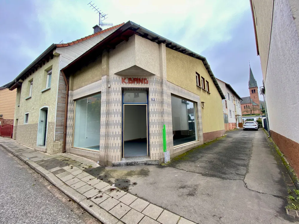 Exterior view of a vacant commercial building with large windows and a door, "K.BANG" sign above the entrance, on a cloudy day.