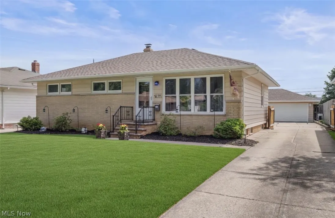 A tan brick and siding single-story home with a green lawn and a detached garage on a sunny day.