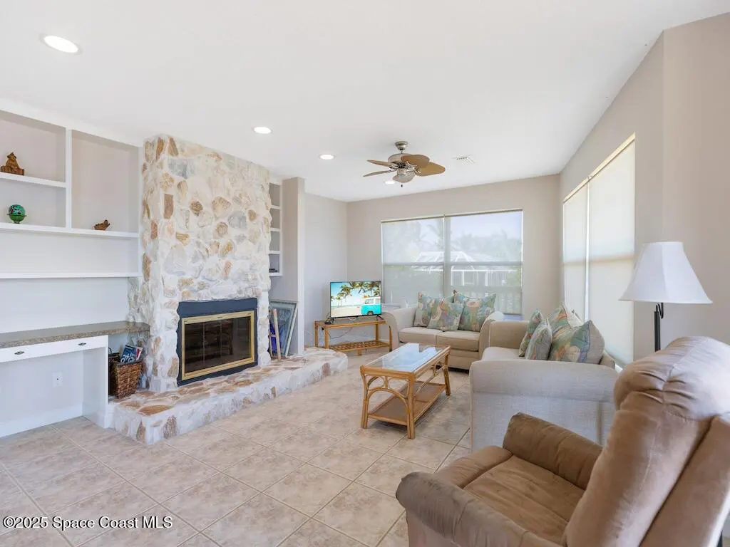 Living room with a stone fireplace, built-in desk, beige sofa, brown recliner, and a coffee table on tiled floors.