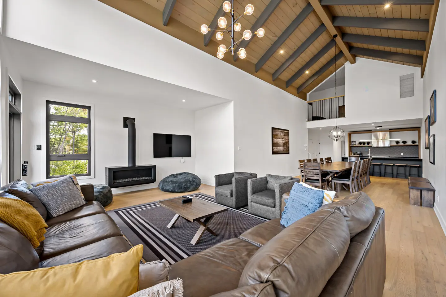 Open-concept living room with vaulted wood ceiling, brown leather sofas, fireplace, and dining area.