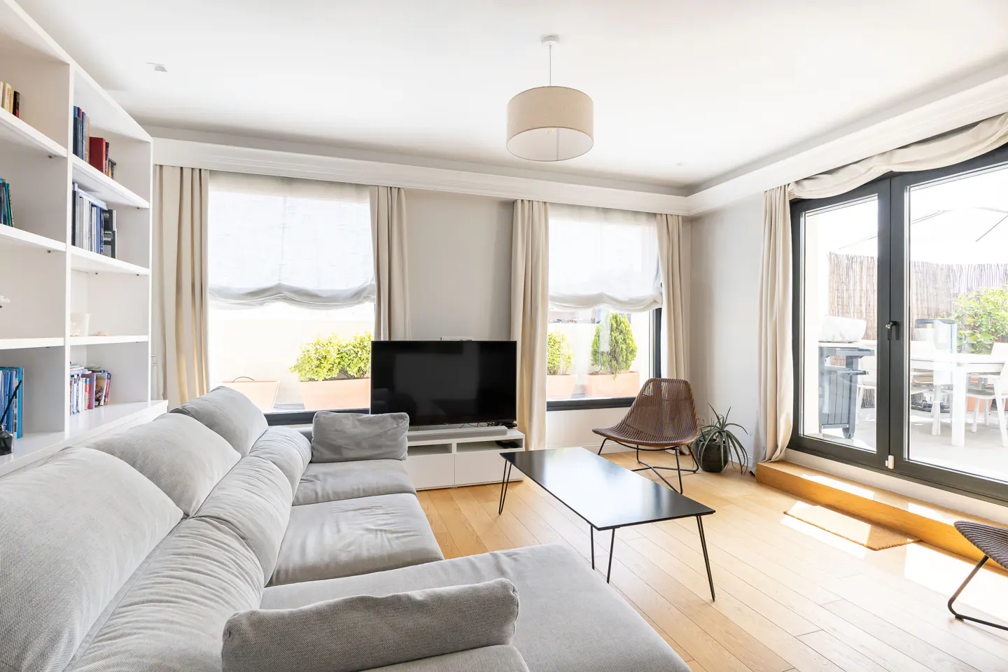Bright living room with a large grey sectional sofa, black coffee table, TV, built-in bookshelf, and patio access.