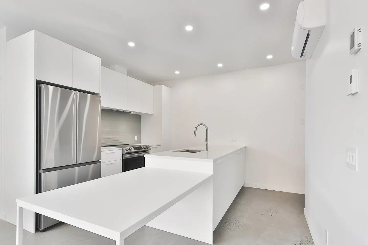 Bright, modern kitchen with white cabinets, stainless steel fridge and oven, and a large white island with a sink and table extension.