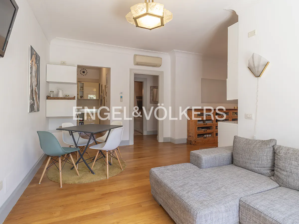 A bright living room with a gray sofa, a black table with four chairs, and wooden floors.