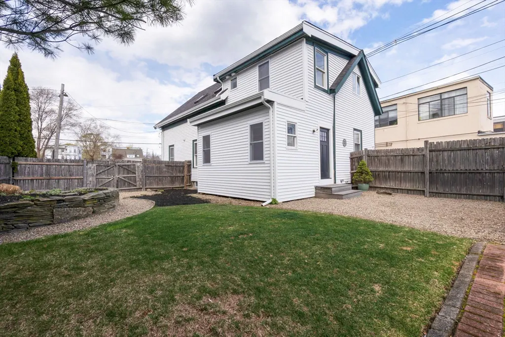 A white two-story house with a green lawn and a wooden fence. The house has a black door and green trim.
