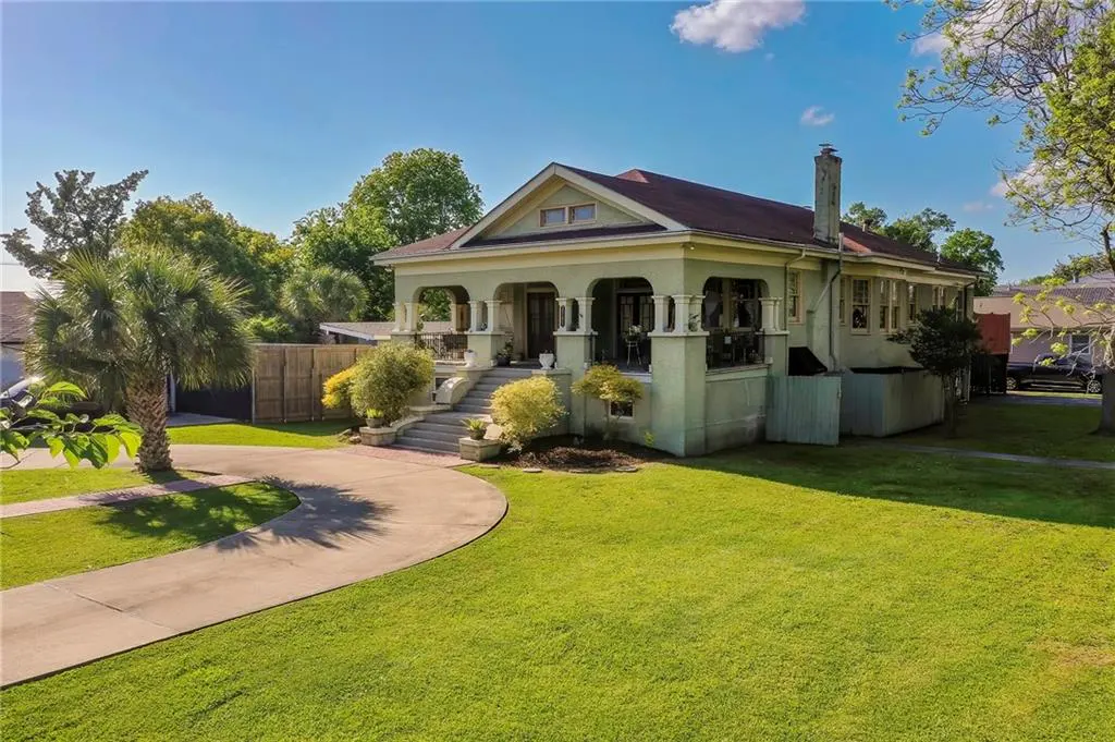 Exterior of a light green house with a red roof, columns, and a large lawn.