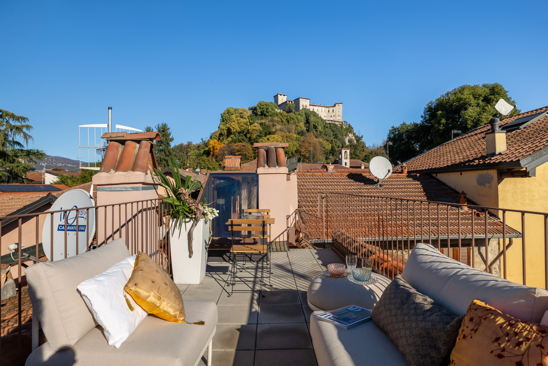 Rooftop patio with seating, potted plants, and a view of a castle on a hill under a clear blue sky.