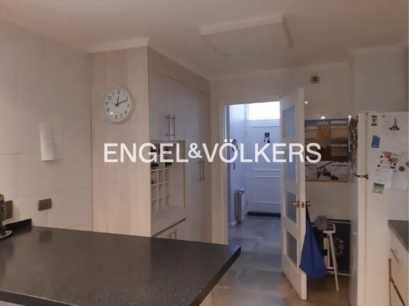 Modern kitchen with dark countertops, light wood cabinets, a wall clock, and an open doorway leading to a hallway.
