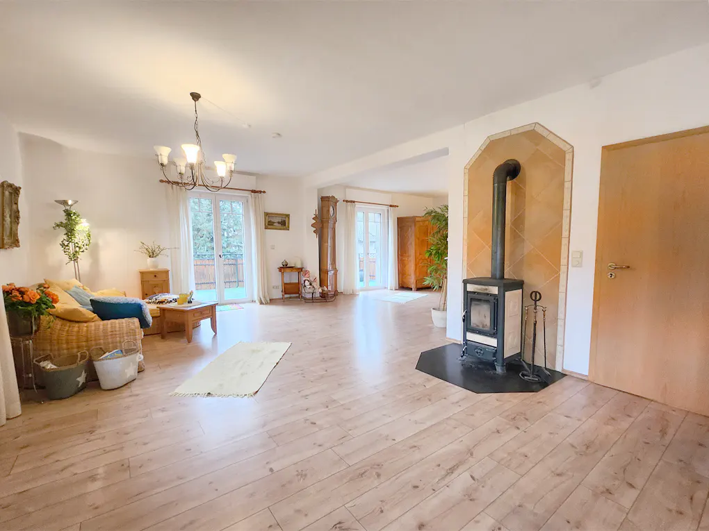 Bright, open living room with wood floors, a fireplace, and a wicker sofa with blue pillows. French doors lead to a balcony.