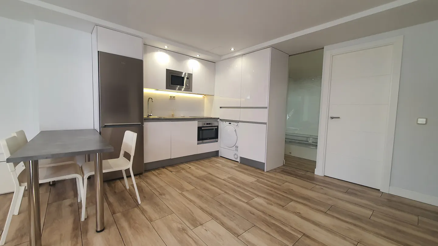 Modern kitchen with white cabinets, stainless steel appliances, wood-look flooring, and a small dining table with two chairs.