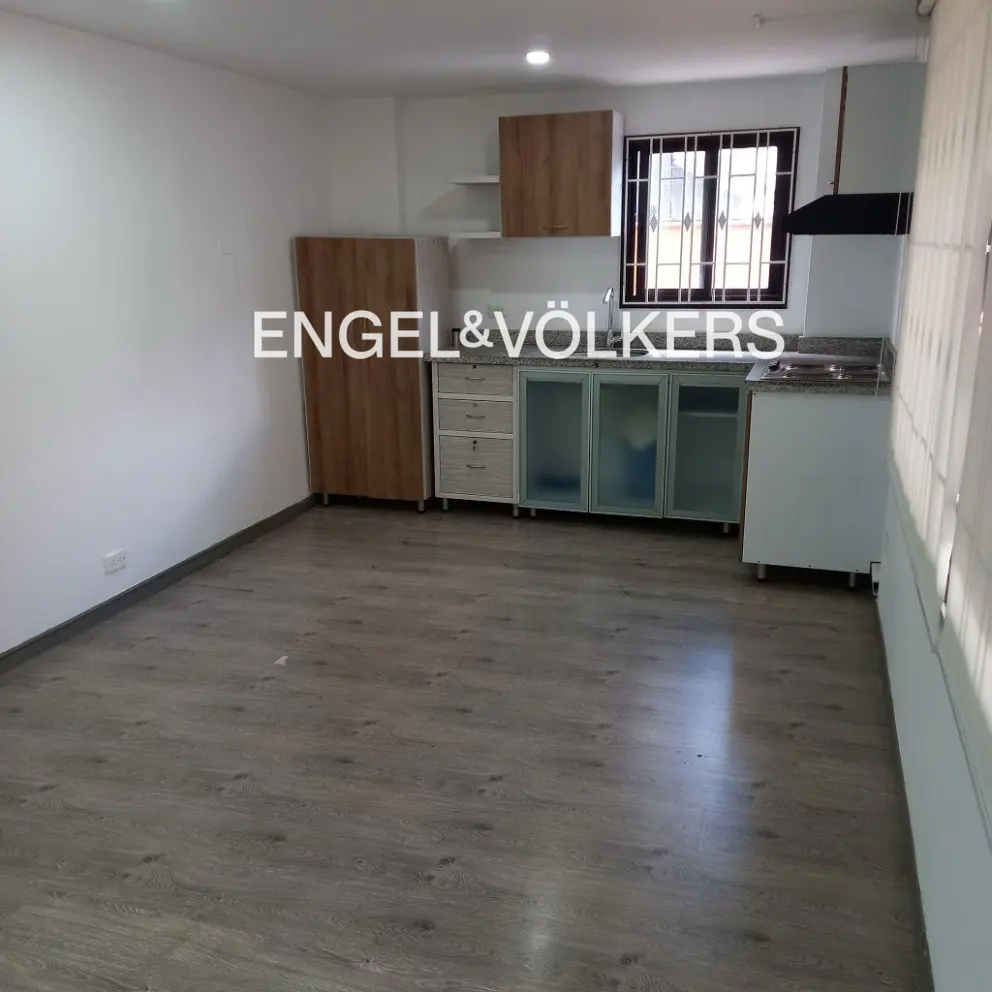 A bright, empty kitchen with wood-look flooring, cabinets, and a window. The Engel & Völkers logo is superimposed on the image.