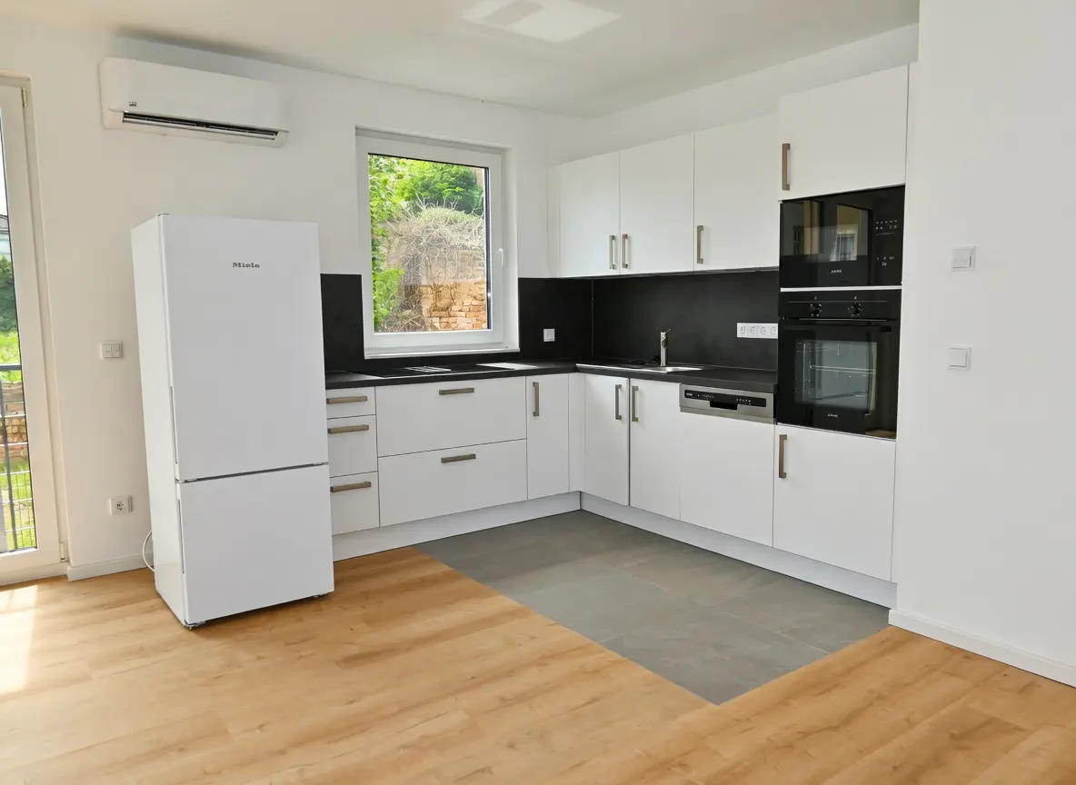 Bright kitchen with white cabinets, black countertops, and stainless steel appliances. Wood and gray tile flooring. Window view of greenery.