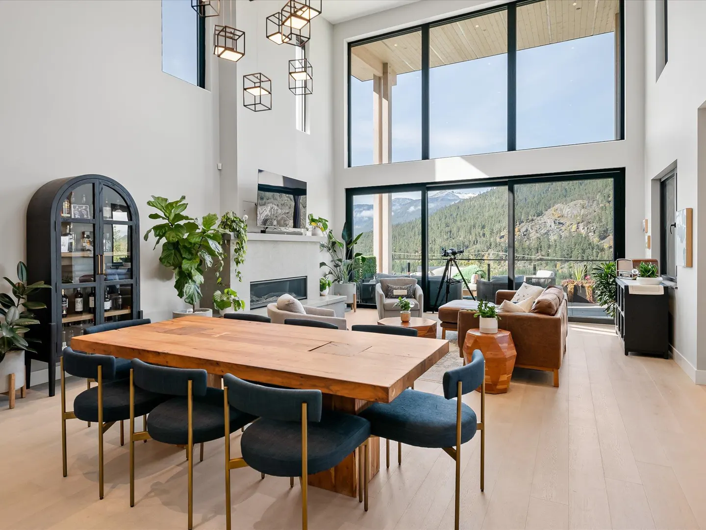 Bright, open-concept living space with a wood dining table, blue chairs, and floor-to-ceiling windows showcasing a mountain view.