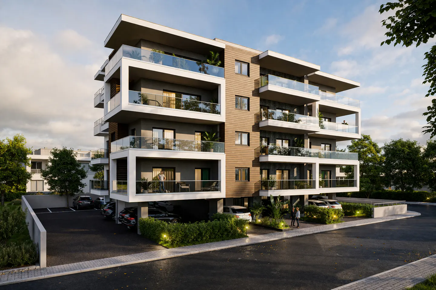 Modern apartment building with white balconies and glass railings, surrounded by greenery and parked cars.