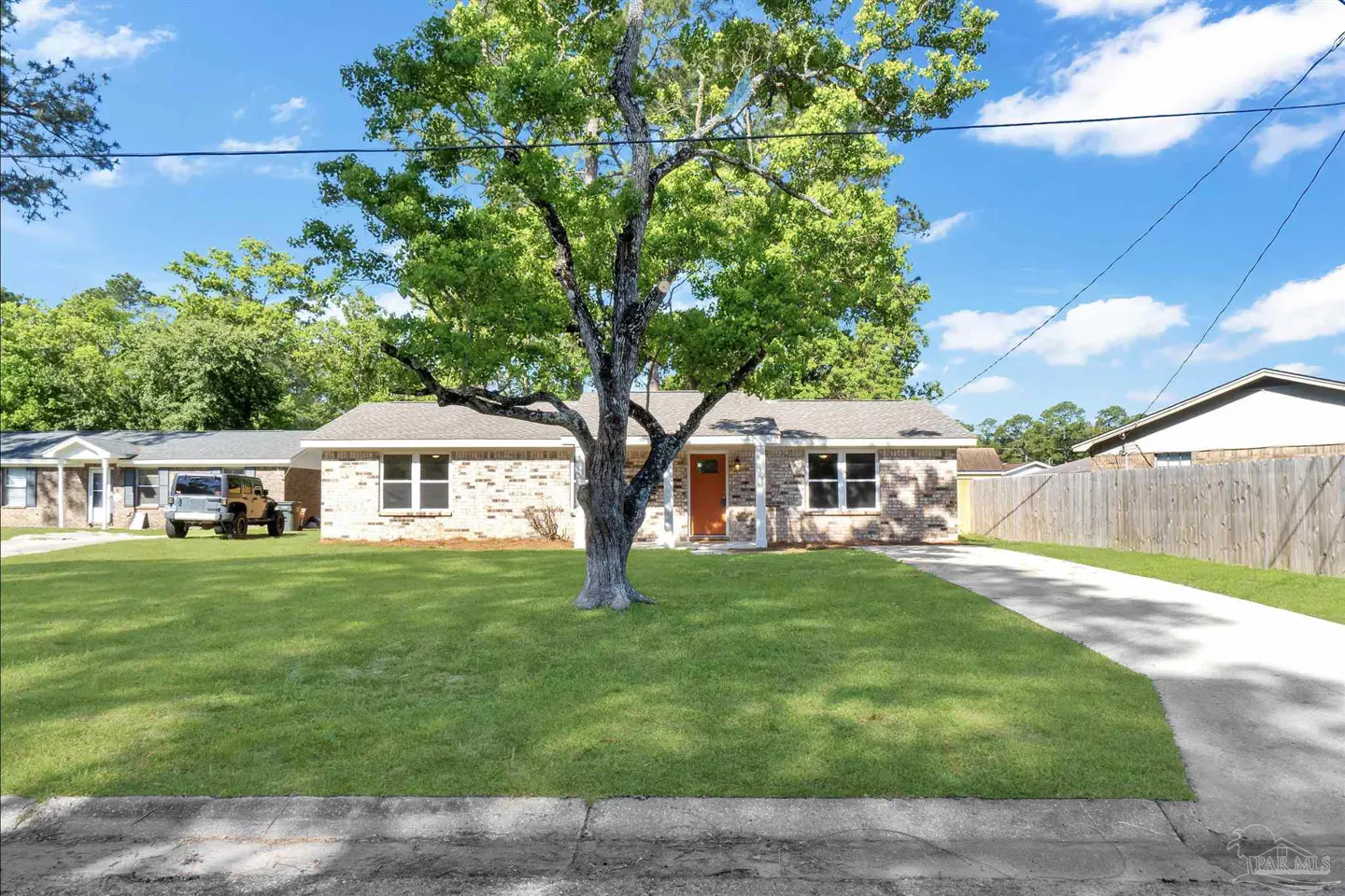 A single-story brick house with an orange door and a large tree in the front yard.