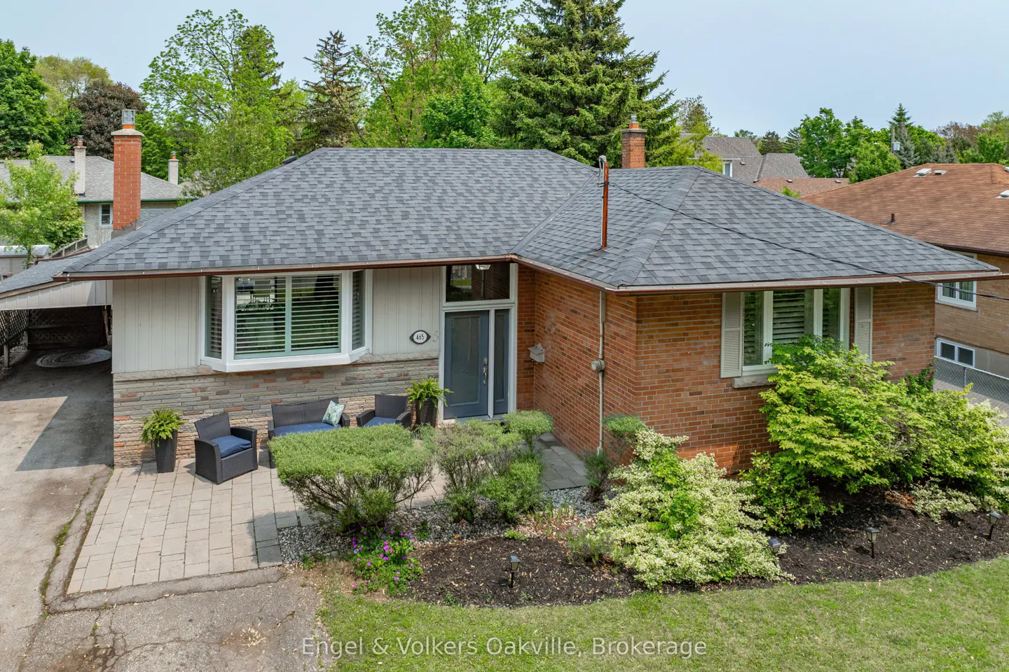 Single-story brick and siding house with a grey shingled roof, front patio furniture, and landscaped front yard.