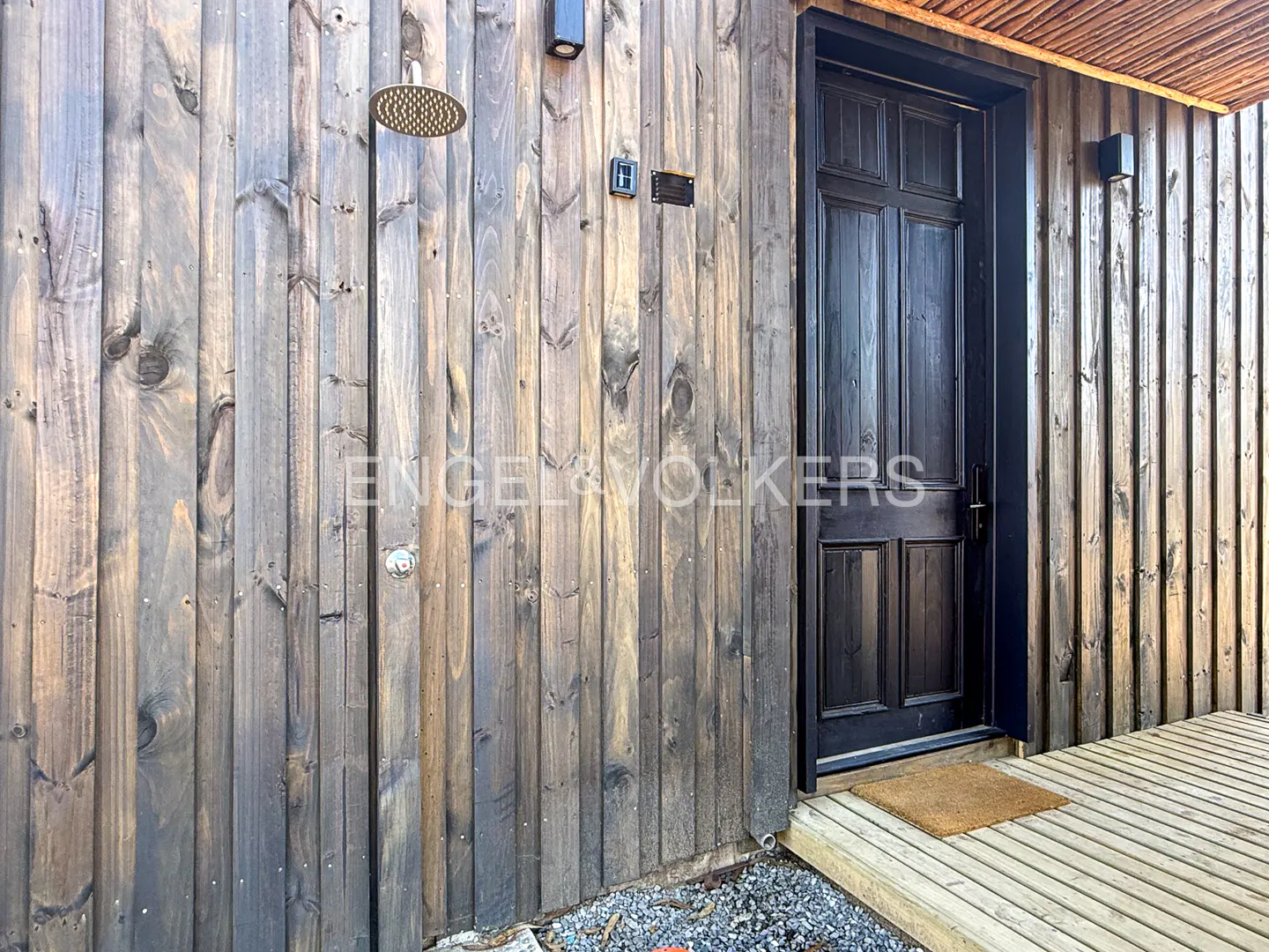 Exterior view of a modern home with a dark wood door, outdoor shower, and wooden deck.