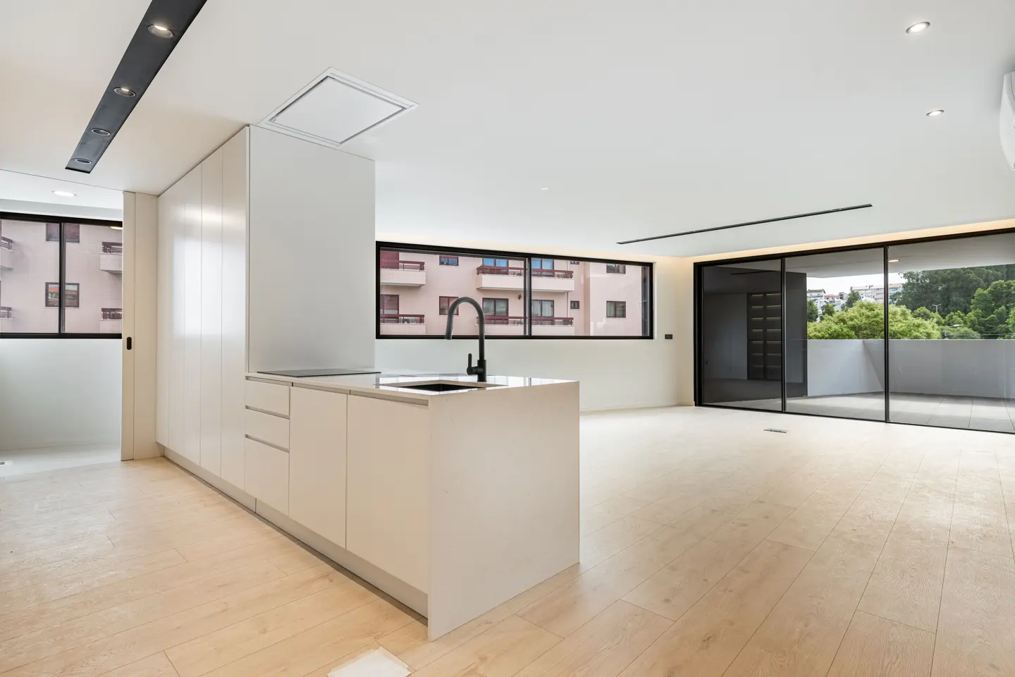 Modern open-plan kitchen with white cabinetry, a black faucet, and light wood flooring, leading to a balcony.