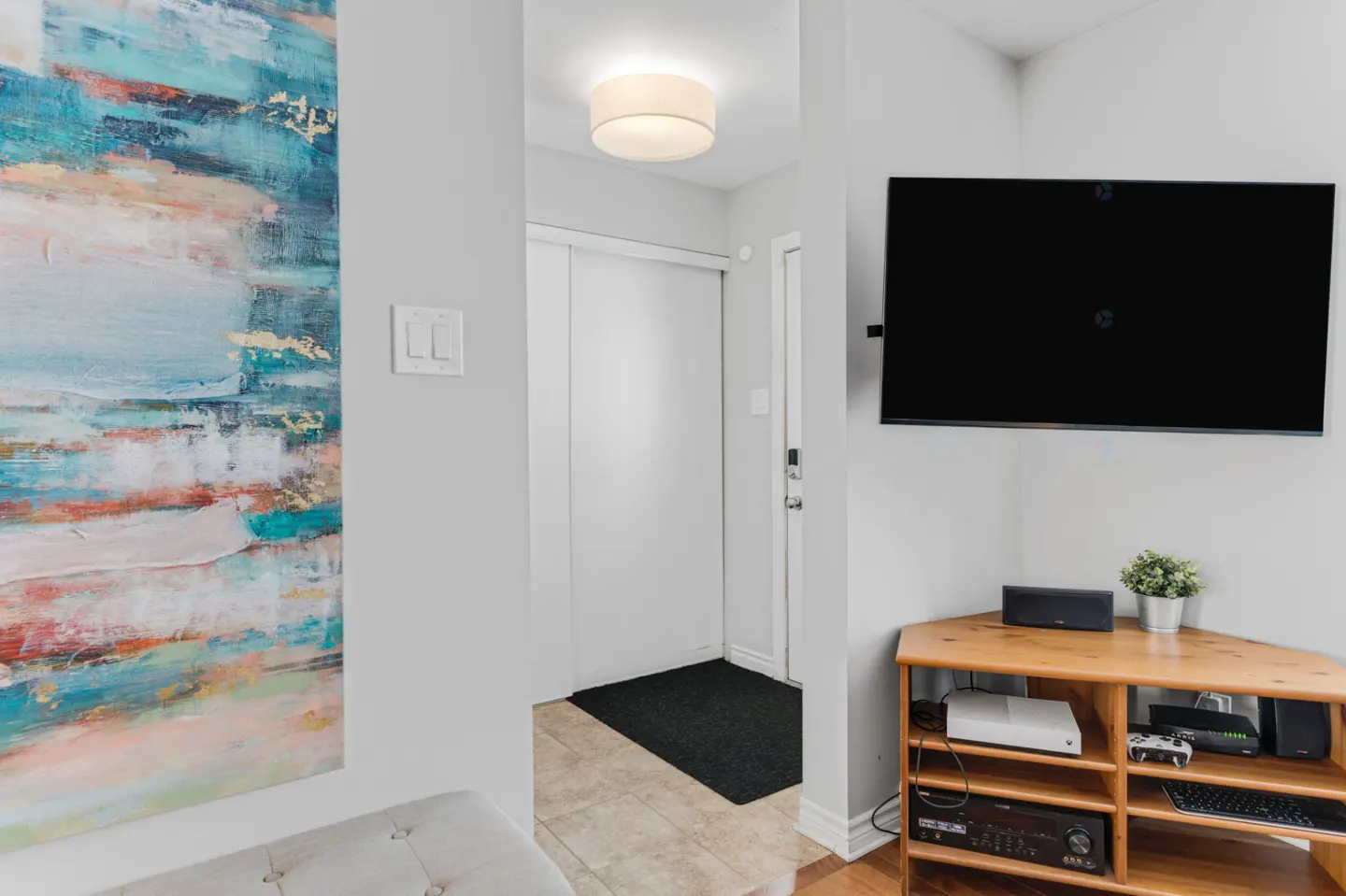 A living room corner with a wall-mounted TV, a wooden media console, and a large abstract blue and gold painting.
