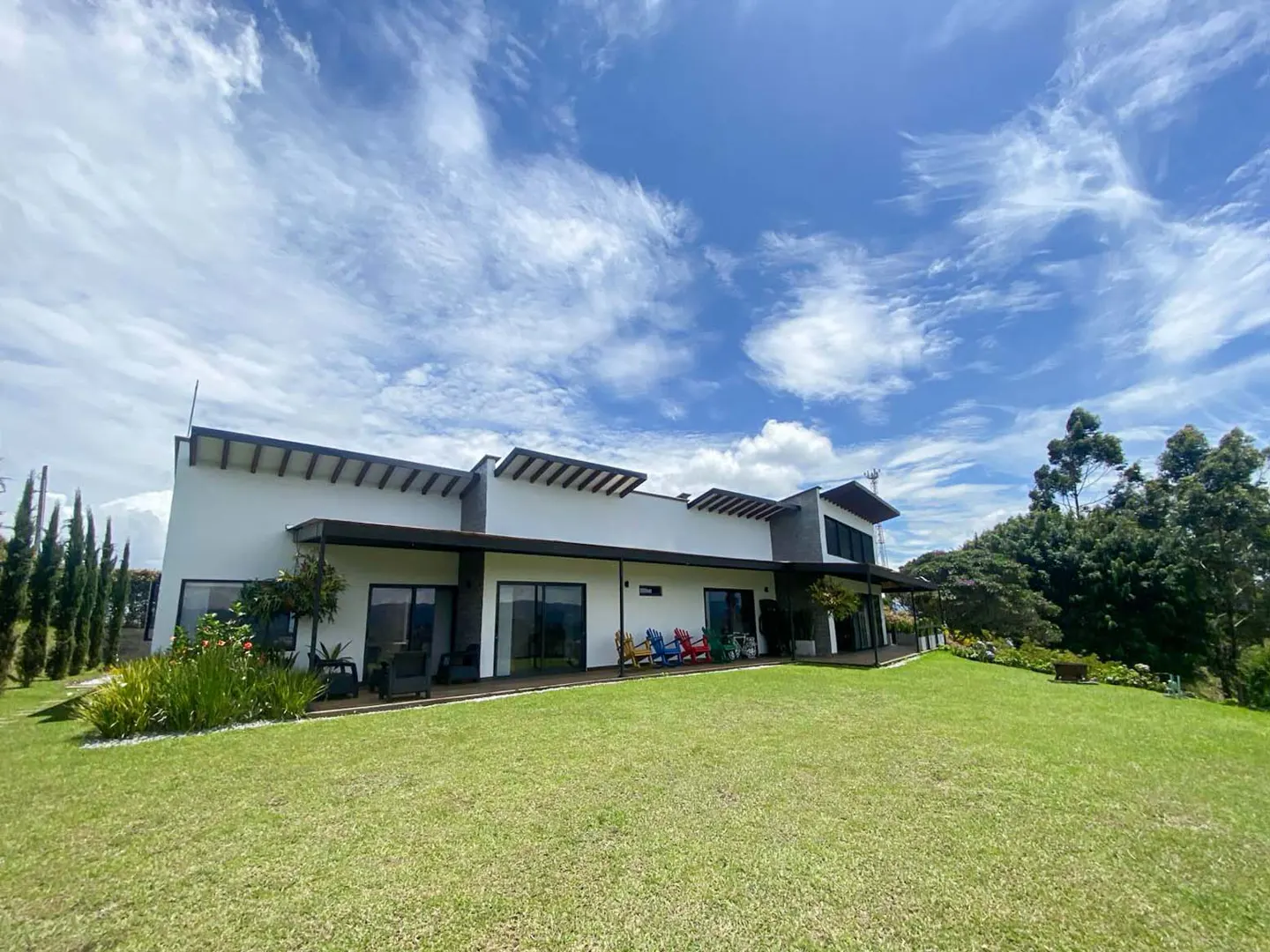 Modern white house with a dark roof, a green lawn, and a blue sky with white clouds.