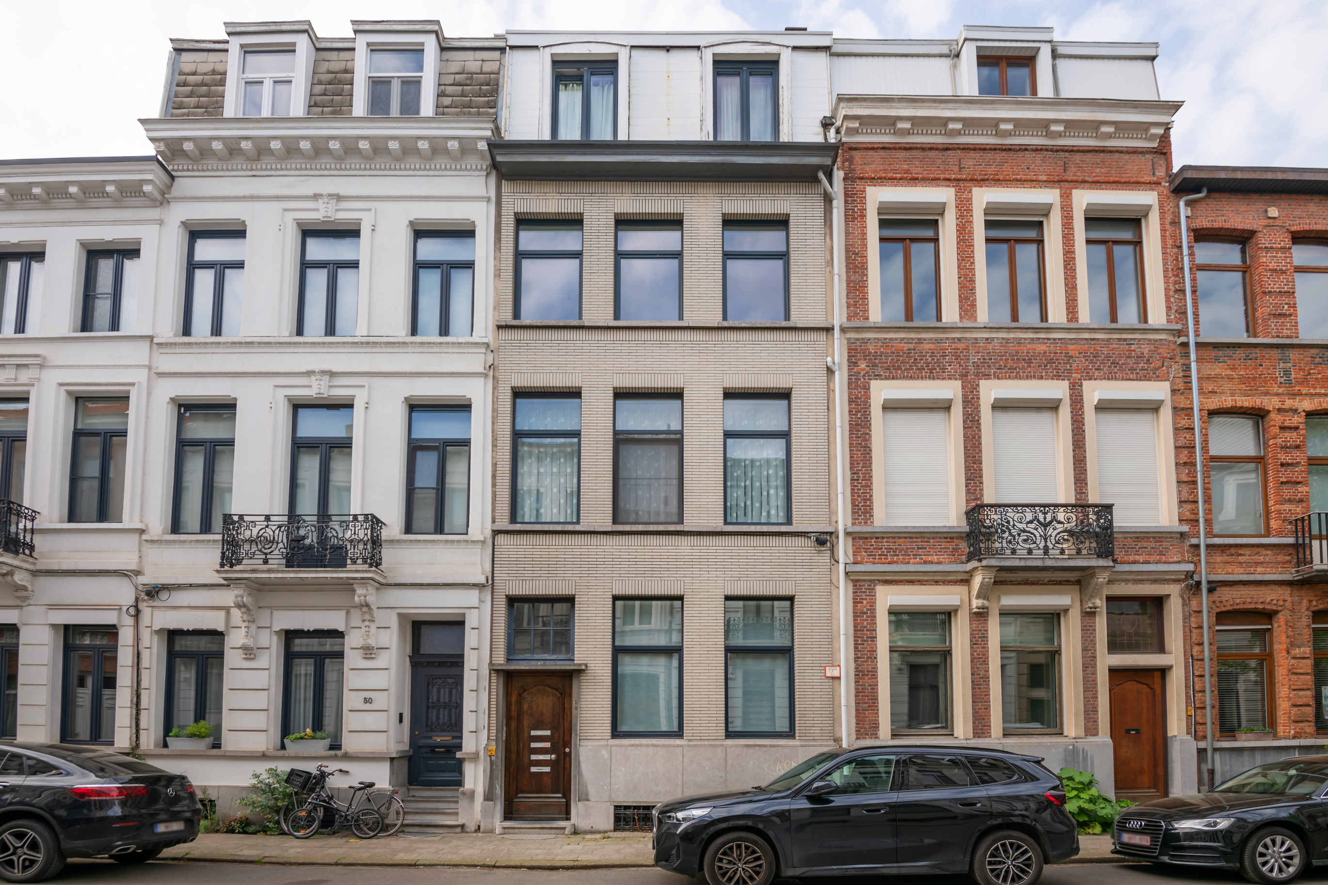 A row of three historic townhouses in white, beige, and red brick, with black cars parked on the street in front. [AI-generated text]