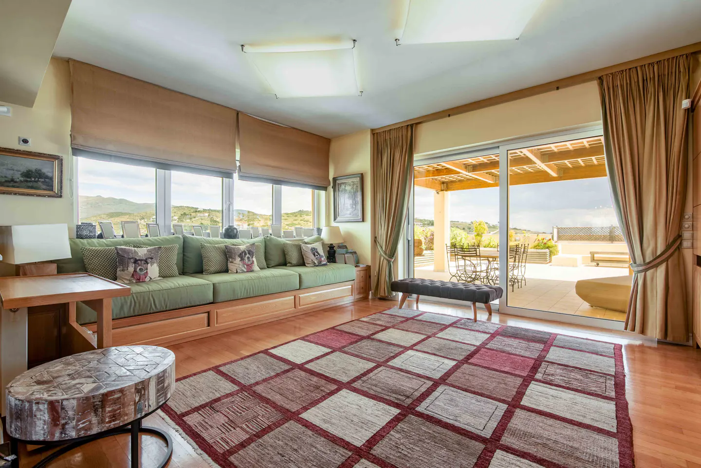 Living room with a green sofa, pillows, and a patterned rug. Sliding glass doors lead to an outdoor patio with furniture.