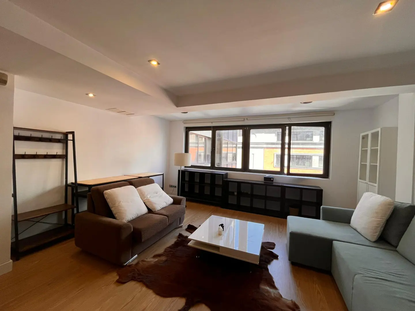 Spacious living room with a brown sofa, light blue sectional, white coffee table, and a cowhide rug on wood flooring.