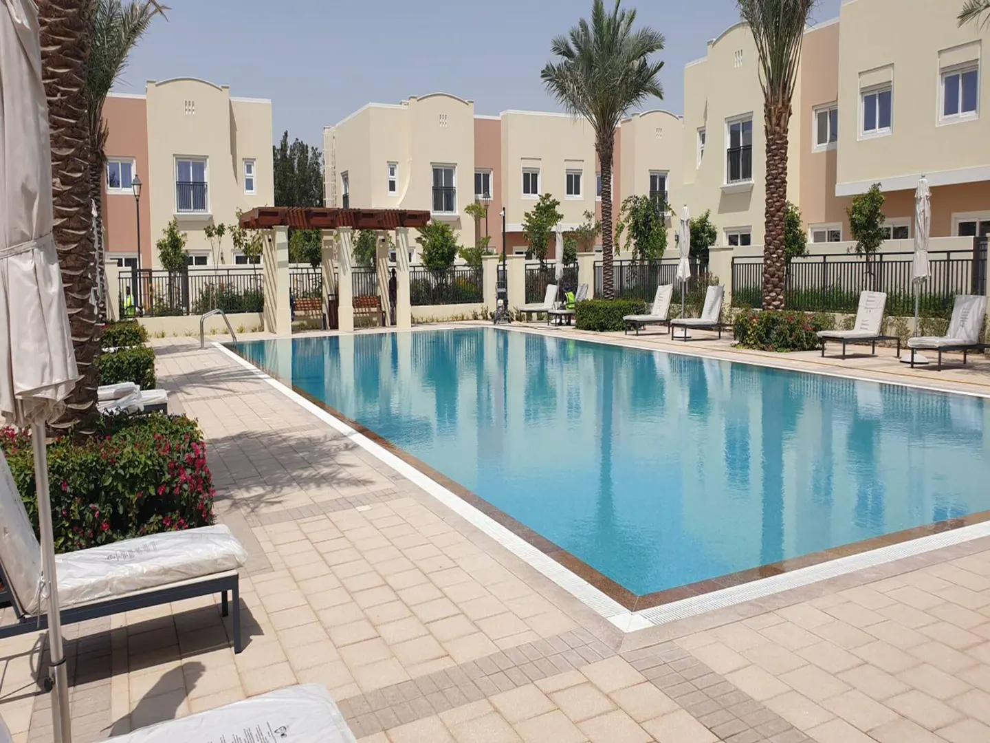 Outdoor pool with lounge chairs and palm trees in a residential community. Beige buildings in the background.