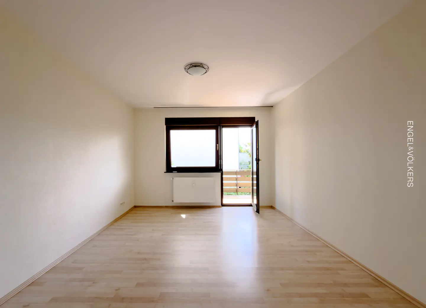 An empty room with light wood floors, white walls, a window, and a door to a balcony.