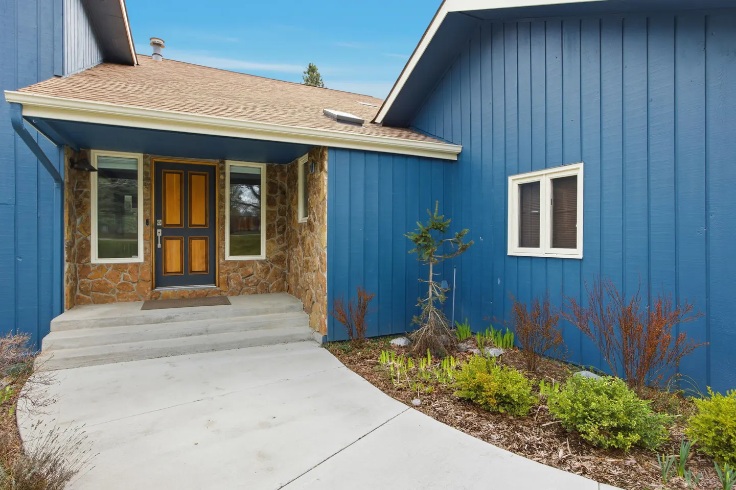 Exterior of a blue house with a stone facade, a brown door, and a concrete walkway.