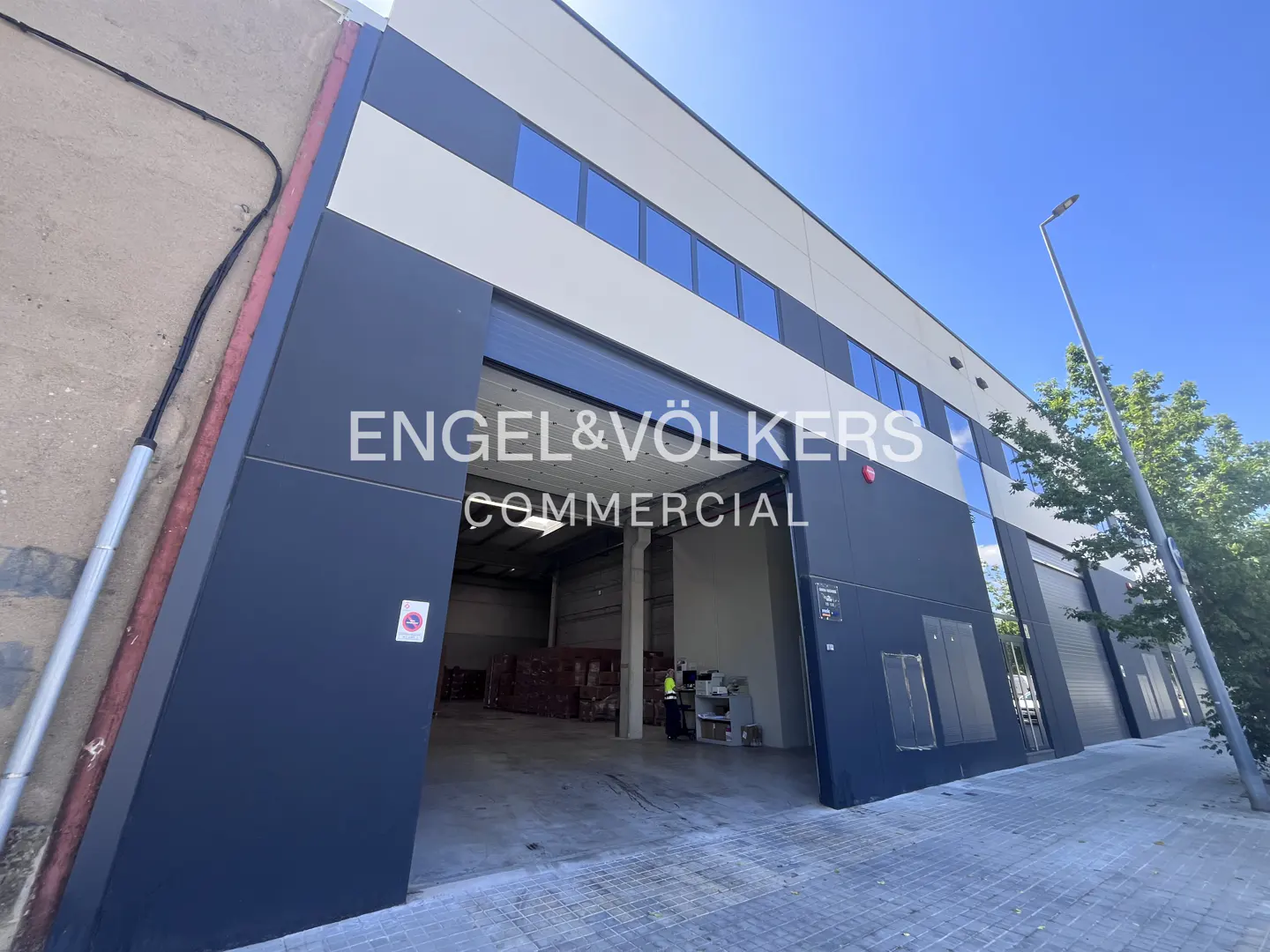 Engel & Völkers commercial building with open loading bay. The building is gray and white with blue windows. A worker is visible inside.