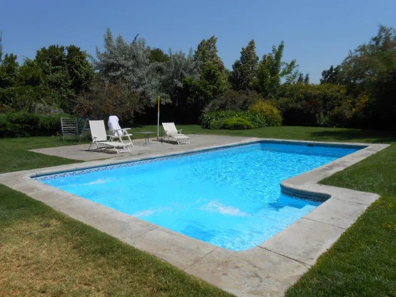 A rectangular in-ground pool with blue water, surrounded by a concrete deck and green grass. Two white lounge chairs sit nearby.