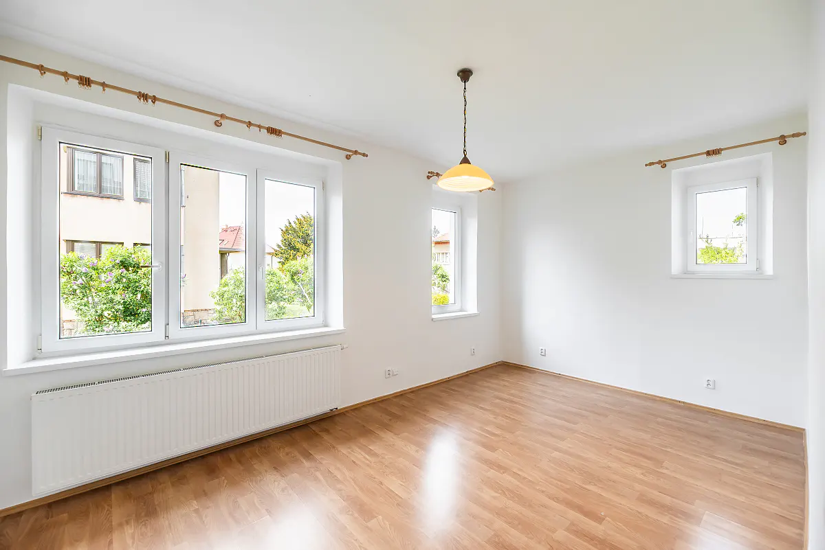 Bright, empty room with wood floor, white walls, and three windows. A light fixture hangs from the ceiling.