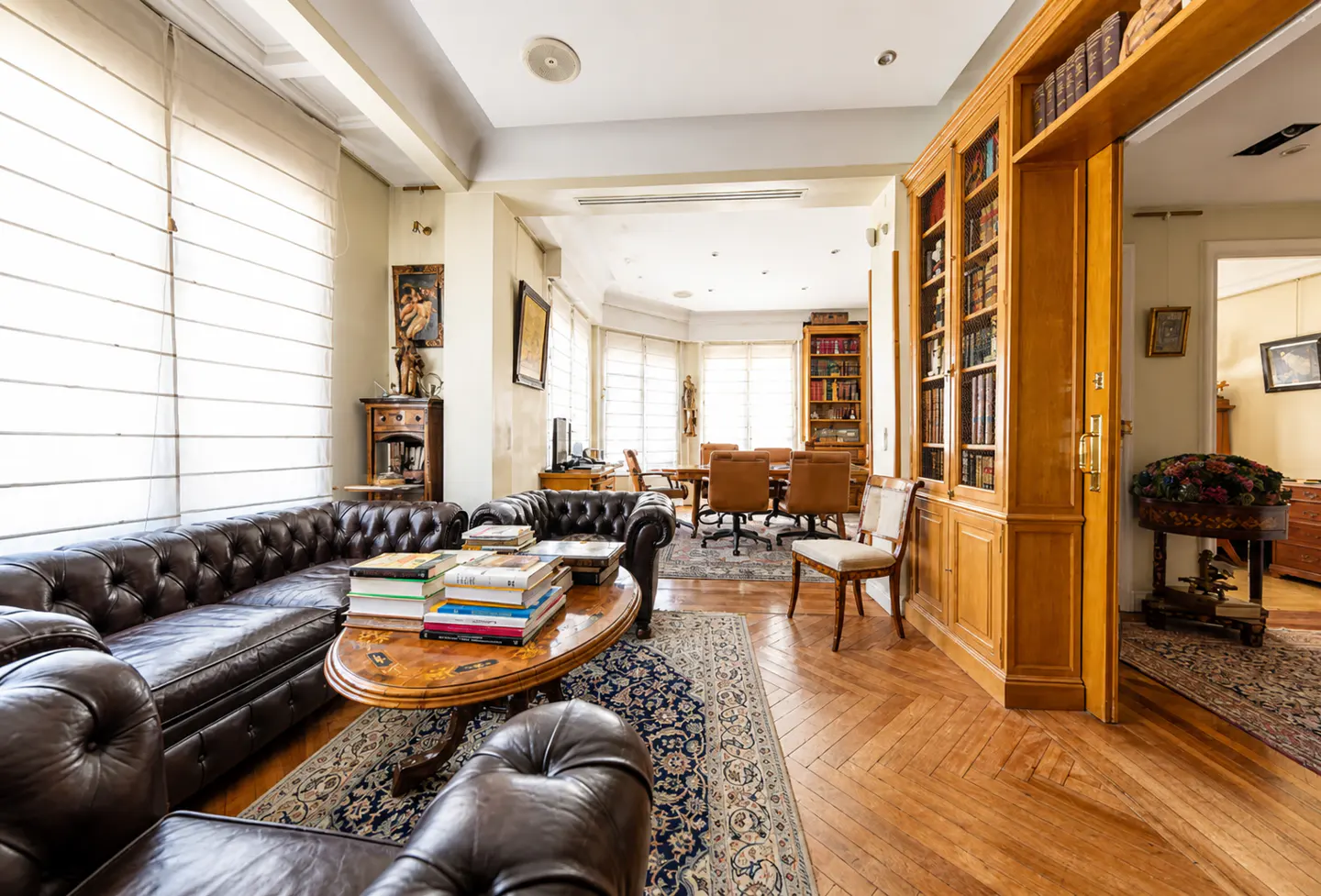 A living room with a brown leather sofa, books on a table, and a wooden bookshelf.