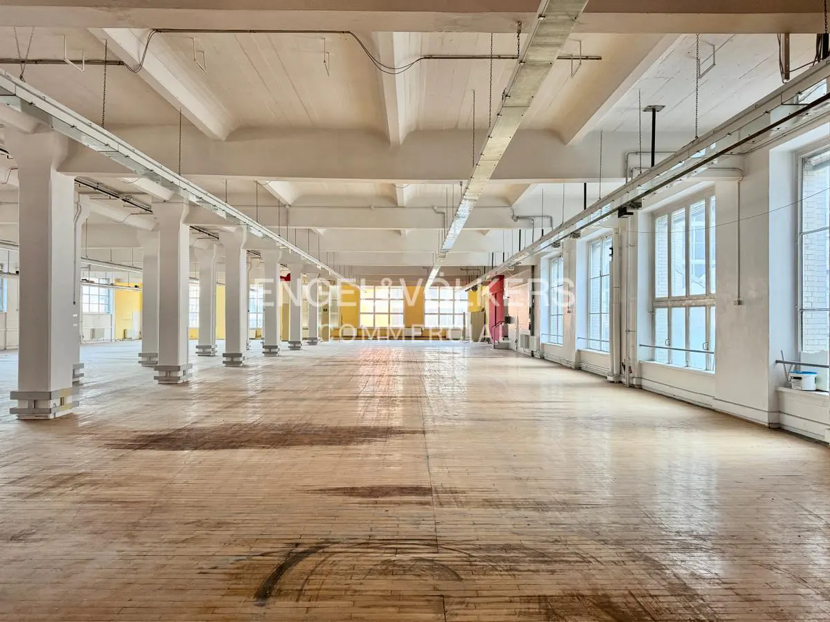 Large, empty commercial space with hardwood floors, white columns, and large windows. The ceiling is high and white.